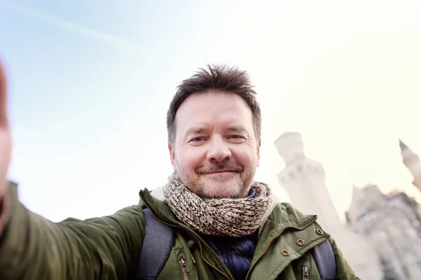 Гарний milddle віці людина робить Автопортрет (selfie) з відомих Королівський замок Нойшванштайн на тлі — стокове фото