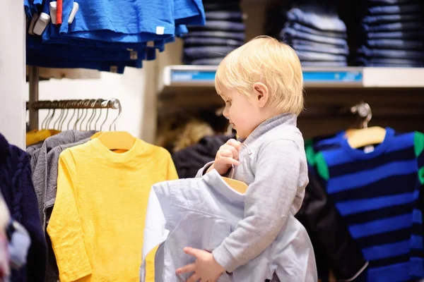 Милый мальчик выбирает новую одежду во время шоппинга — стоковое фото