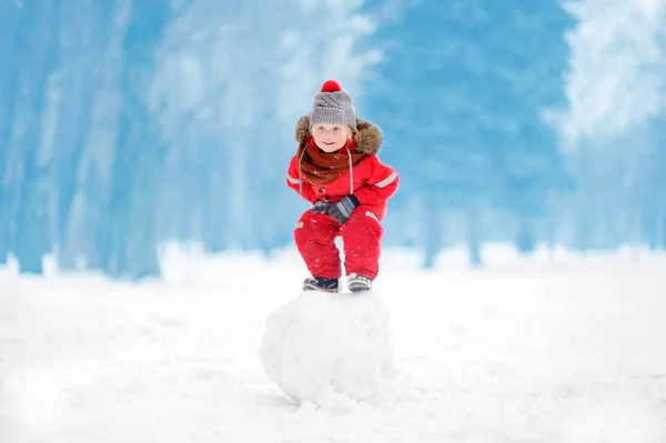 Menino em roupas vermelhas de inverno se divertindo com bola de neve — Fotografia de Stock