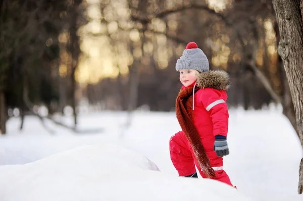 Menino em roupas vermelhas de inverno se divertindo com neve fresca — Fotografia de Stock