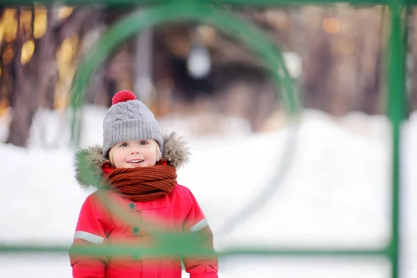 Menino em roupas vermelhas de inverno se divertindo no parque infantil ao ar livre — Fotografia de Stock