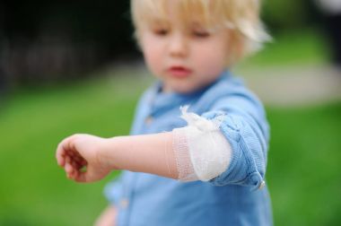 Cute little boy looking on his elbow with applied bandage clipart