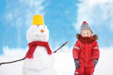 Kardan adam ile eğleniyor karlı parkta kırmızı kış giysileri içinde küçük çocuk