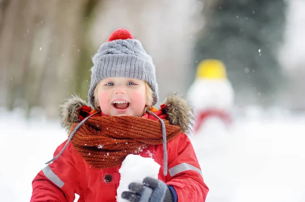 Little boy playing with snowballs with snowman on background — Stock Photo, Image