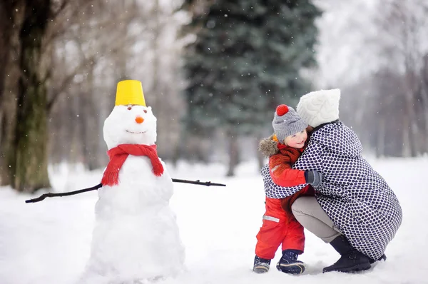 Little boy with his mother/babysitter/grandmother building snowman in snowy park — Stock Photo, Image