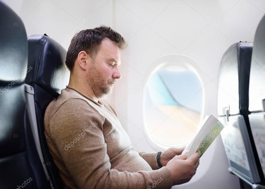 Middle age man traveling by an airplane and reading a book during the flight. Transportation concept