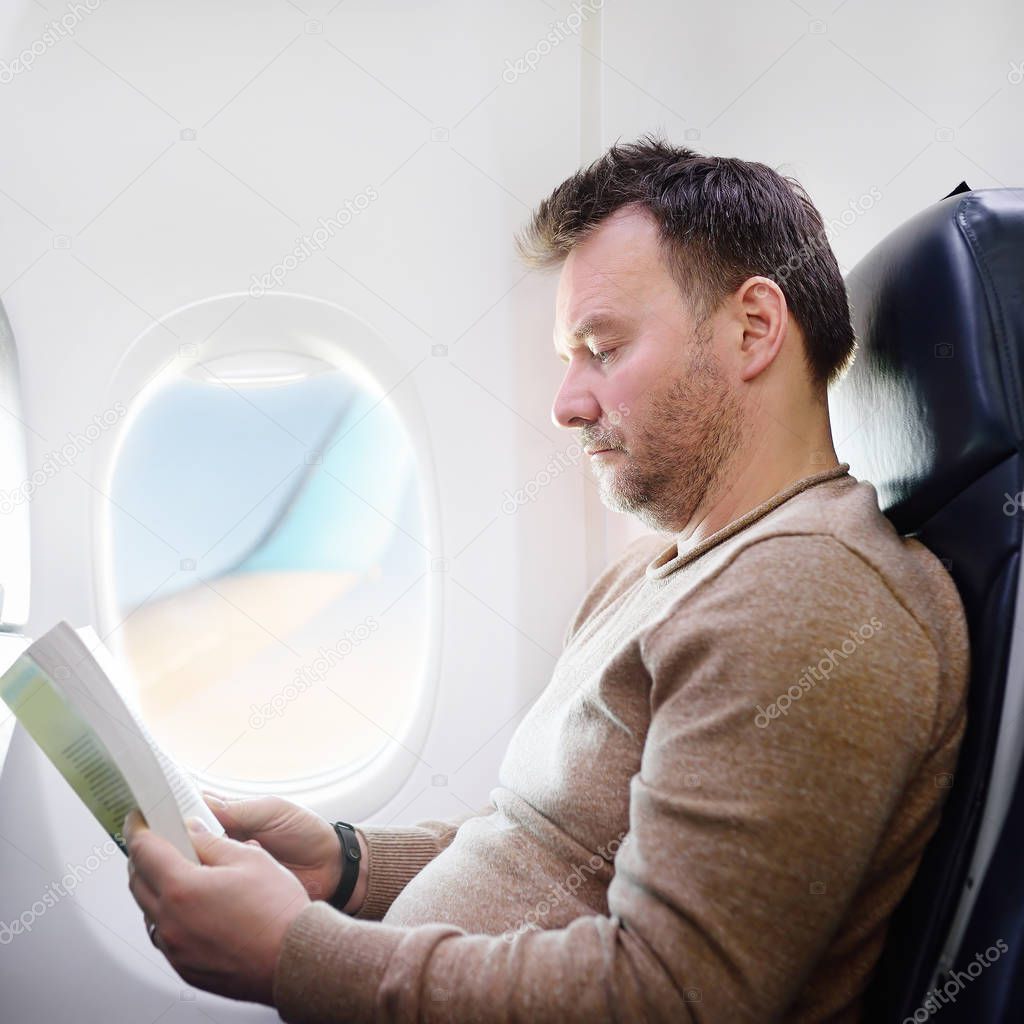 Middle age man traveling by an airplane and reading a book during the flight. Transportation concept