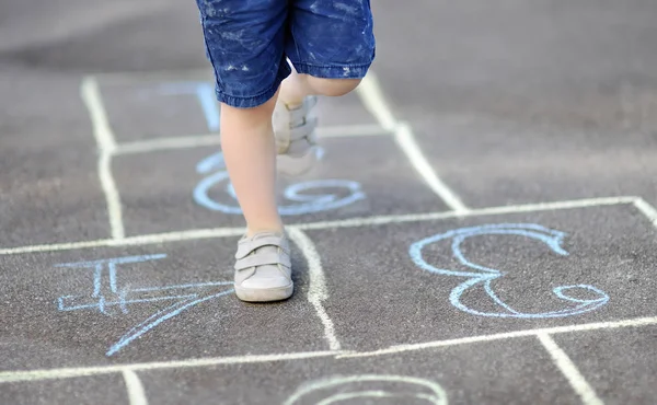 Closeup of little boy's legs and hopscotch drawn on asphalt — Stock Photo, Image