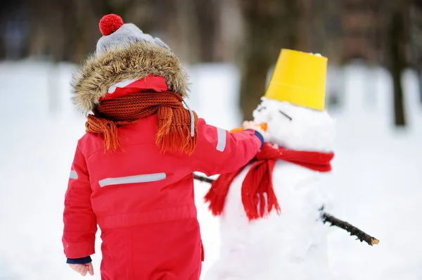 雪の公園で雪だるまを楽しんで赤冬の服の少年 — ストック写真
