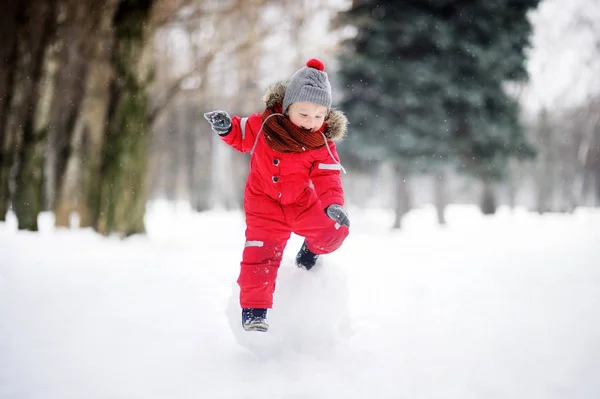 Menino em roupas vermelhas de inverno se divertindo com bola de neve — Fotografia de Stock