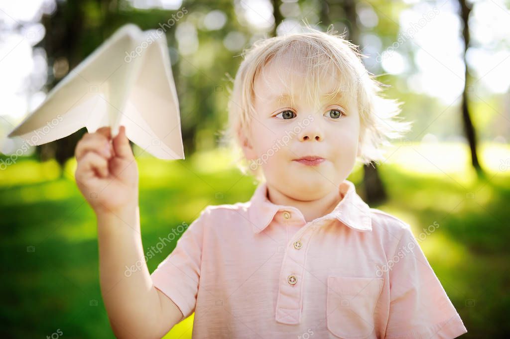 Cute toddler boy playing with paper plane in a summer park