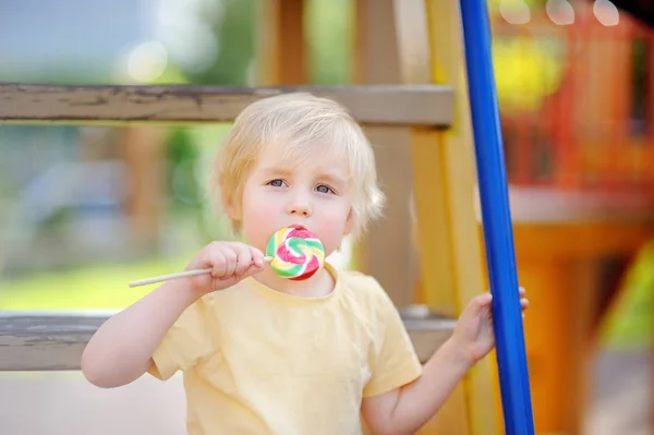 Piccolo ragazzo divertirsi e mangiare grandi lecca-lecca sul parco giochi all'aperto — Foto Stock