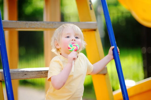 Piccolo ragazzo divertirsi e mangiare grandi lecca-lecca sul parco giochi all'aperto — Foto Stock