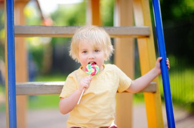 Eğlenceli sahip ve açık sahada büyük lolipop yemek küçük çocuk