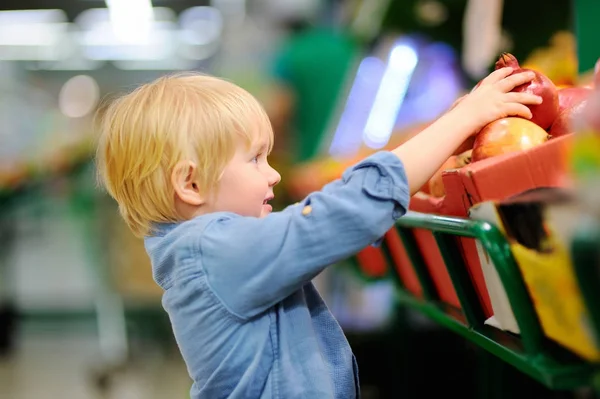 Aranyos kisfiú egy élelmiszer-áruház vagy egy szupermarket, friss bio gránátalma kiválasztása — Stock Fotó