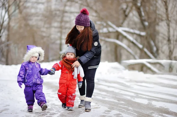 Young asian woman helping caucasian toddler boy anf girl with their winter clothes — Stock Photo, Image