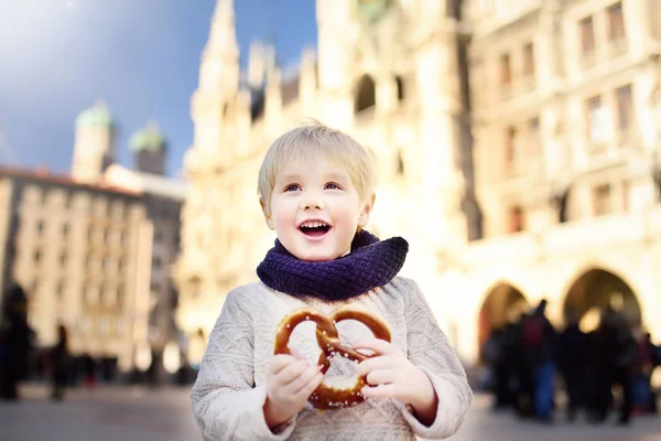 Kleiner Tourist mit traditionellem bayerischem Brot namens Brezel auf dem Hintergrund des Rathauses in München, Deutschland — Stockfoto