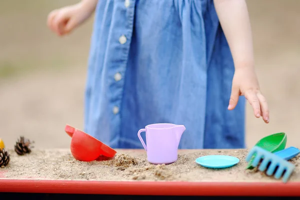 Niedliches Kleinkind spielt im Sandkasten mit Formen und Tannenzapfen — Stockfoto