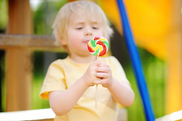 Liten pojke att ha kul och äta stora lollipop på lekplatsen utomhus — Stockfoto