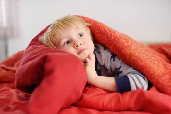 Menino bonito de pijama se divertindo na cama depois de dormir e assistir TV ou sonhando — Fotografia de Stock