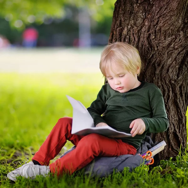 Roztomilý malý školák sedí pod stromem a studovat. Zpět do — Stock fotografie