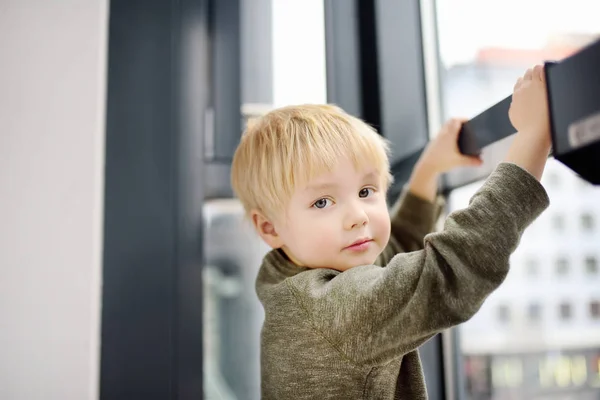 Ihana pieni poika istuu ikkunassa lähellä panoraamaikkunaa ja katselee ulos — kuvapankkivalokuva
