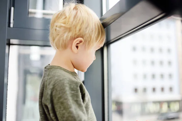 Lovely little boy sitting on the window near panoramic window and looking outside — Stok fotoğraf