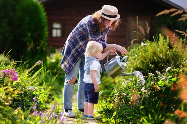 Menino e sua jovem mãe regando plantas no jardim — Fotografia de Stock