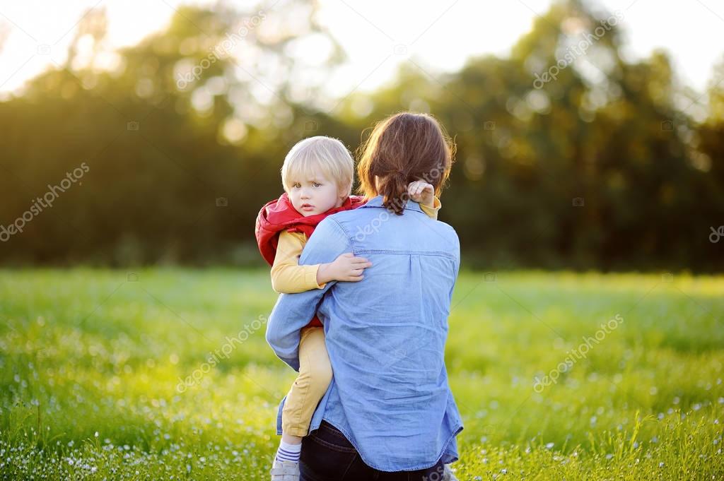 Young mother holding her little son during walk in the flowers field