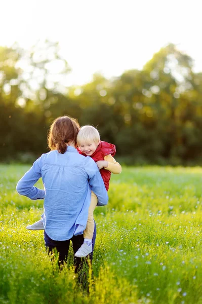 Junge Mutter hält ihren kleinen Sohn beim Spaziergang im Blumenfeld — Stockfoto