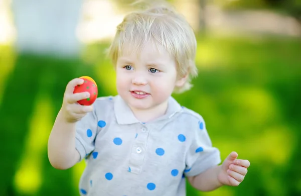 Malý chlapec loví velikonoční vejce v jarní zahradě o velikonočním dni — Stock fotografie