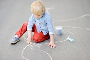 Mutlu küçük çocuk çocuk ile renkli tebeşir asfalt üzerinde çizim.