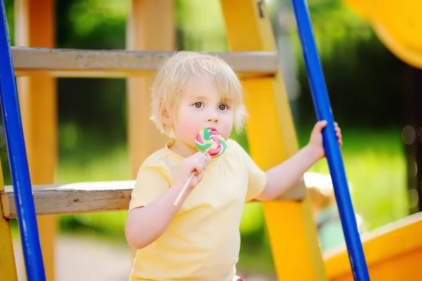 Menino se divertindo e comendo grande pirulito no playground ao ar livre — Fotografia de Stock
