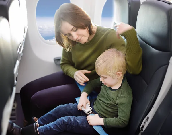 Молодая мать помогает своему маленькому сыну с ремнем безопасности во время путешествия на самолете — стоковое фото