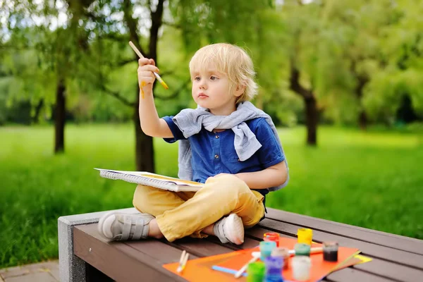 Schattige kleine jongen tekenen met kleurrijke verf in zomer park — Stockfoto