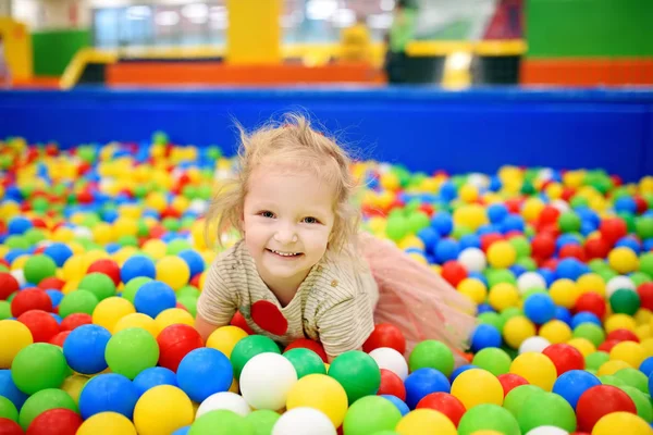 Ragazzina riccia divertirsi nella buca della palla con le palle colorate — Foto Stock