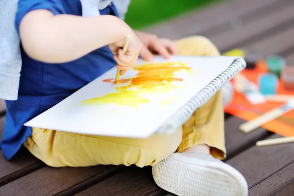 Милий маленький хлопчик малює барвистими фарбами в літньому парку — стокове фото