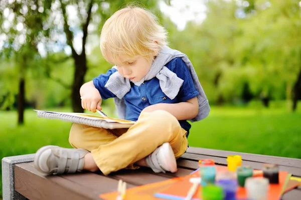 Симпатичный маленький мальчик рисует красочными красками в летнем парке — стоковое фото