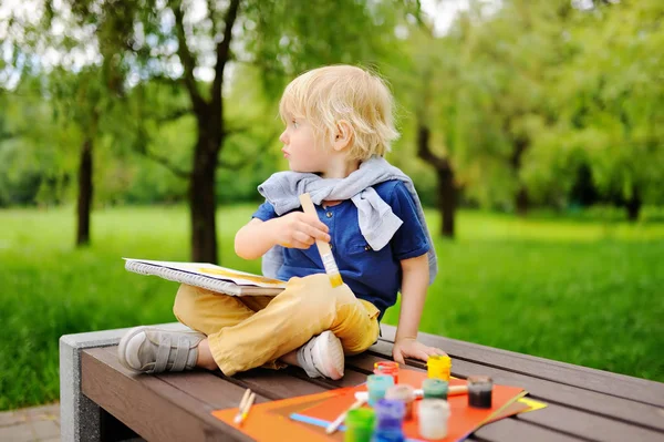 Cute little boy drawing with colorful paints in summer park Stock Picture