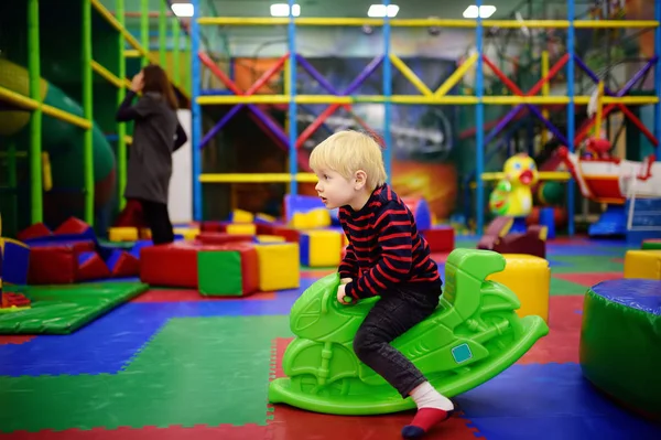 Fröhlicher kleiner Junge hat Spaß mit Plastikspielzeug-Schaukel / hüpfendem Motorrad im Spielcenter — Stockfoto