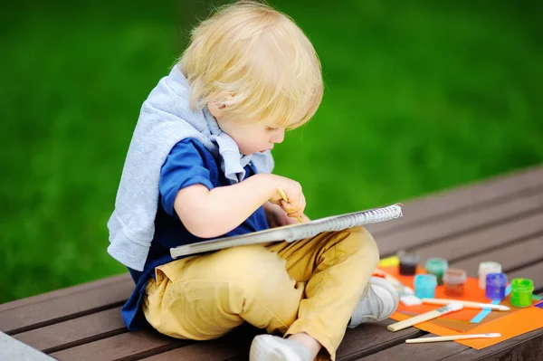 Cute little boy drawing with colorful paints in summer park Stock Image