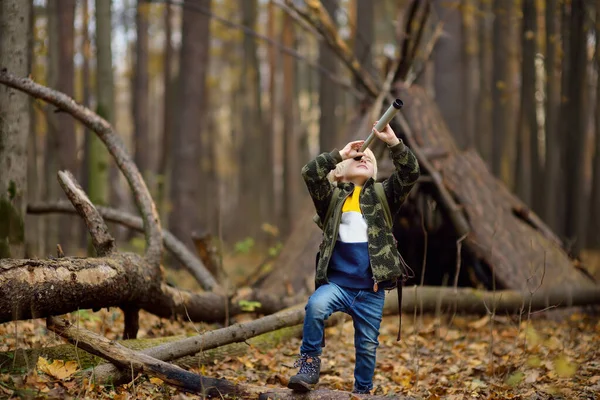 秋の森の中でハイキング中にスパイガラス付きの小さな男の子スカウト。子供はスパイガラスを通して見ている. — ストック写真