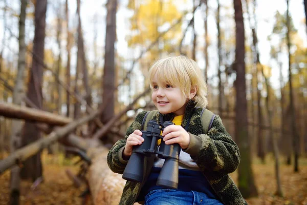 Pfadfinder mit Ferngläsern beim Wandern im Herbstwald. Kind sitzt auf großem umgestürzten Baum und blickt durch Fernglas. — Stockfoto