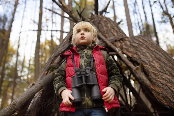 Malý skaut s dalekohledem během túry v podzimním lese. Za dítětem je teepee hut. — Stock fotografie