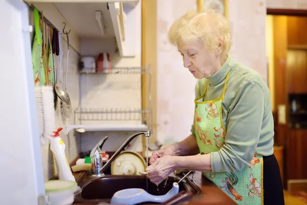 Portrait de femme âgée aux cheveux blancs bouclés. Une dame âgée lave la vaisselle dans la cuisine à la maison . — Photo