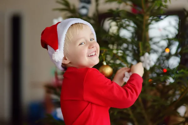 小男孩戴着圣诞礼帽,准备庆祝圣诞节. 可爱的孩子用玻璃玩具装饰圣诞树 — 图库照片