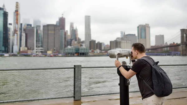 Tourist looks through binoculars to the Manhattan skyline over East River in rainy day. — Stock Photo, Image