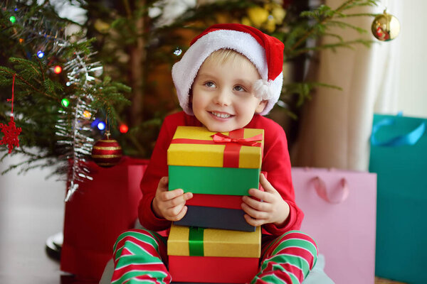 Excited little boy with a Christmas gift under fir tree at home. Portrait of happy kid in Christmas morning.