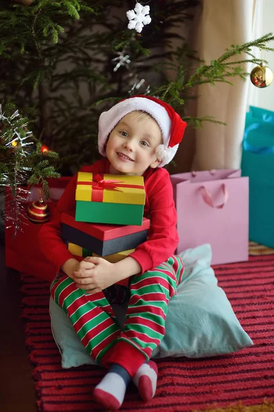 Podekscytowany chłopiec z prezentem świątecznym pod choinką w domu. Portret szczęśliwego dziecka w świąteczny poranek. — Zdjęcie stockowe