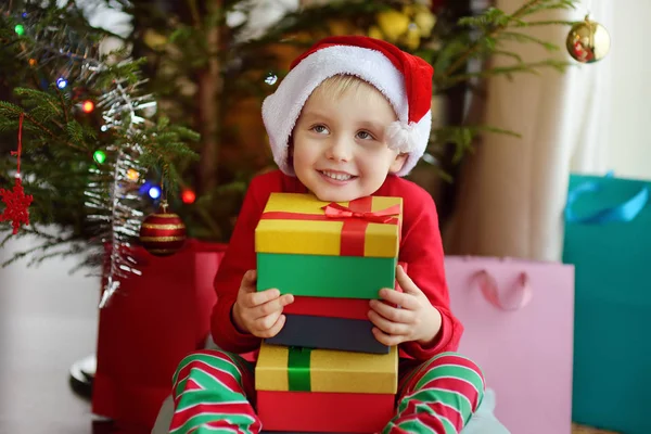 Excited little boy with a Christmas gift under fir tree at home. Portrait of happy kid in Christmas morning. Stock Picture